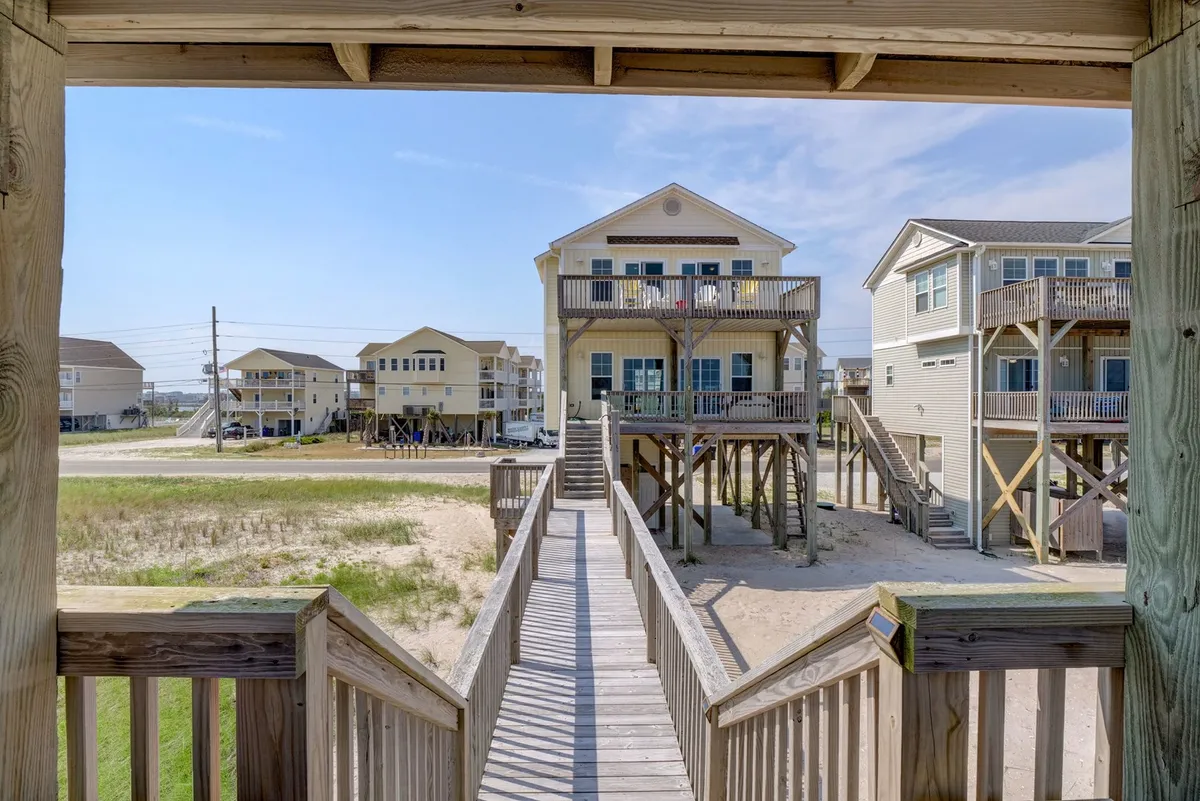 This image shows a wooden walkway leading towards the beach, flanked by beach houses and a sandy area. The atmosphere is relaxed, suggesting a place where families can gather and set out for beach outings. The view captures a sense of openness and the inviting nature of the surrounding coastal community, perfect for strolls or starting an adventure on Topsail Island.