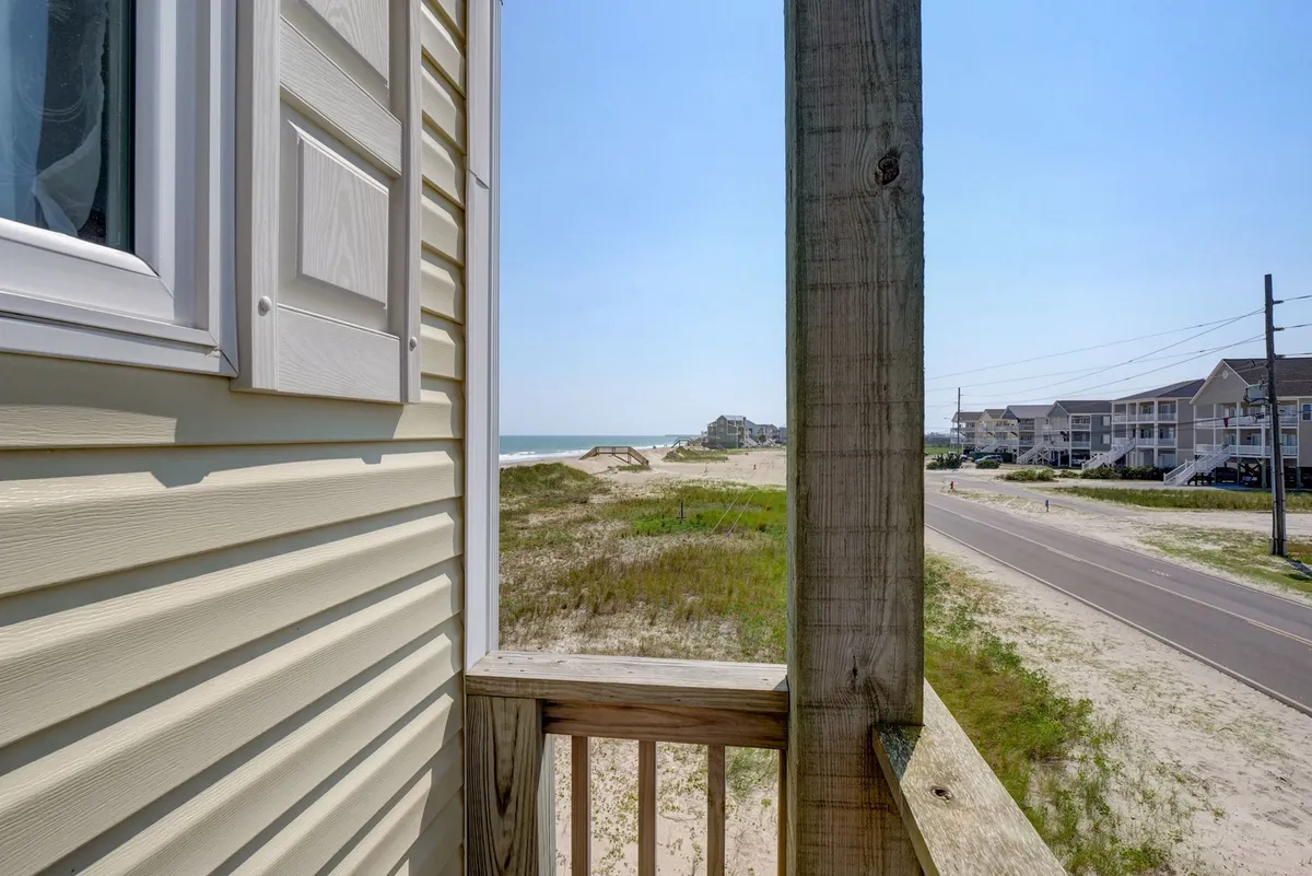 This image features a stunning ocean view framed by a coastal dune landscape and a wooden railing, inviting thoughts of beachcombing, sunbathing, and walks along the shore. The relaxed mood and expansive view highlight the natural beauty that guests can experience on Topsail Island.