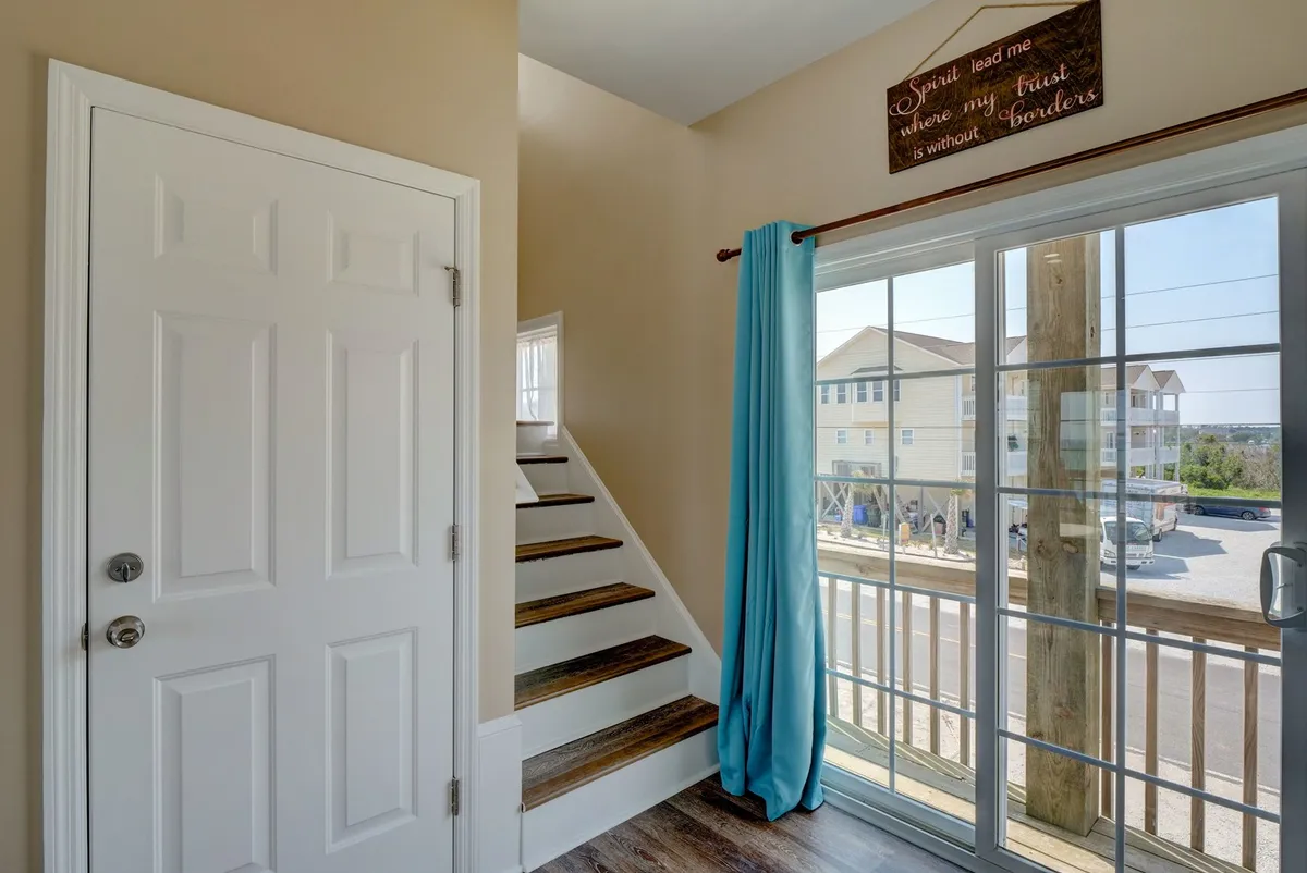 A warm, inviting entryway featuring the front door, a staircase leading upstairs, a large window draped with curtains, and a charming wall sign. Natural light fills the space, creating a welcoming first impression.