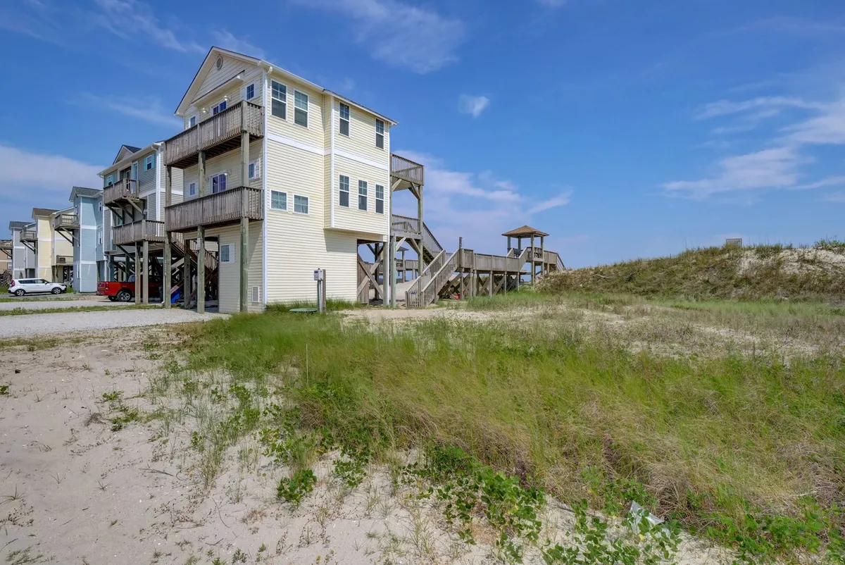 This image highlights the beach house's exterior with a wooden walkway leading directly to the sand, surrounded by lush greenery. The scene evokes the ease of stepping from the house onto the beach, with plenty of space for outdoor family activities and gatherings.